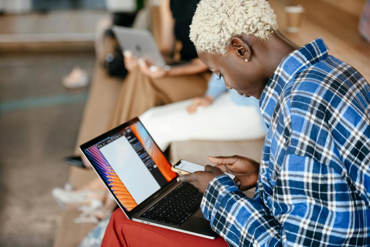 Busy black woman using smartphone while browsing laptop